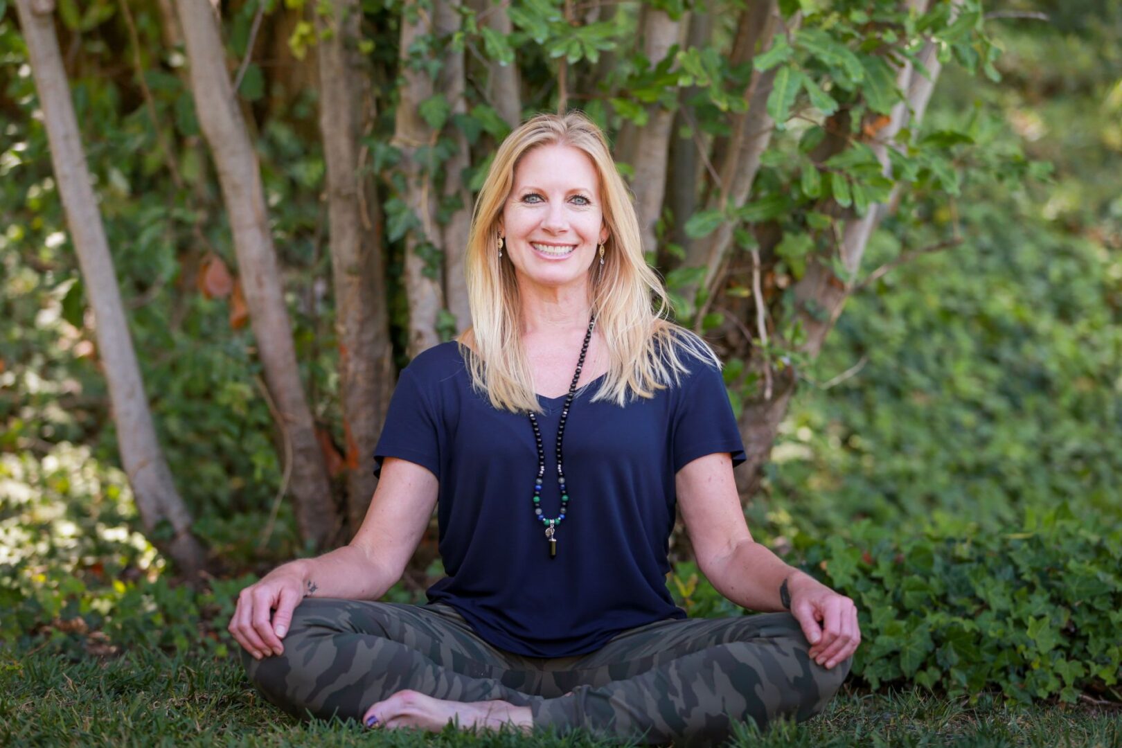 A woman sitting in the grass with her hands on her knees.