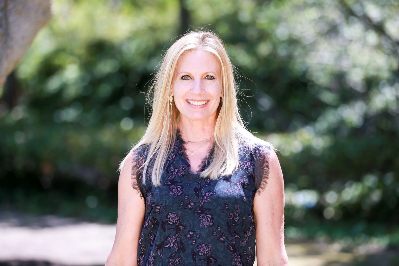 A woman standing in front of trees smiling for the camera.