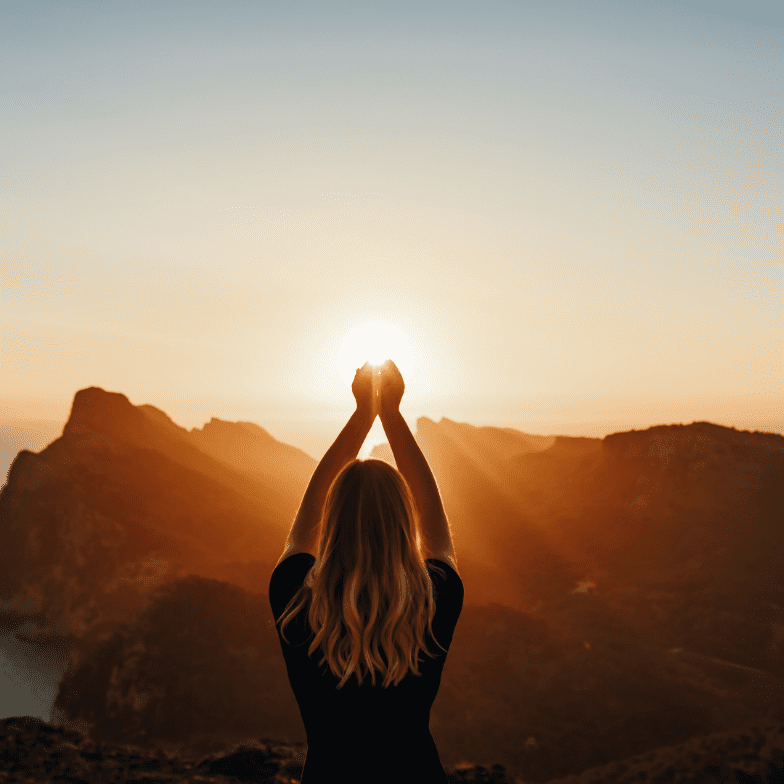 A person standing on top of a mountain with their hands in the air.